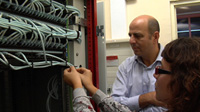 Imagen que muestra a un hombre y una mujer mirando los cables de una instalación. El hombre observa mientras la mujer está arreglando los cables.