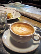 Desayuno con taza de café en primer plano. De fondo un periódico.