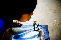 Un niño o niña bebiendo agua que sale de una fuente.