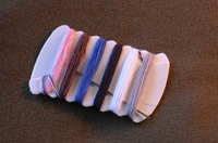 Hilos de colores rosa, marrón, azul, blanco y negro liados en una bobina plana.