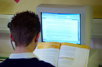 Estudiante sentado de espalda trabajando con ordenador y un libro.