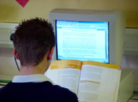 Estudiante sentado de espalda trabajando con ordenador y un libro.