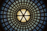 Ilustración en la que se puede ver una lámpara de cristales colgando de una vidriera con forma de domo. Desde la perspectiva parece una tela de araña.