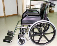 Discapacidad motriz. Ilustración en la que se ve una silla de ruedas en un primer plano situada en una habitación.