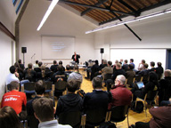 Sala repleta de asistentes, escuchando una ponencia de un programador en un congreso.