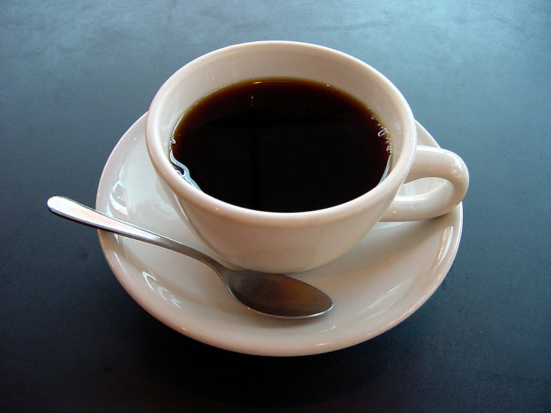 Imagen de primer plano de una taza de café expreso sobre un plato y un fondo negro.  