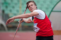 Atleta con camiseta de tirantes roja lanzando una jabalina.