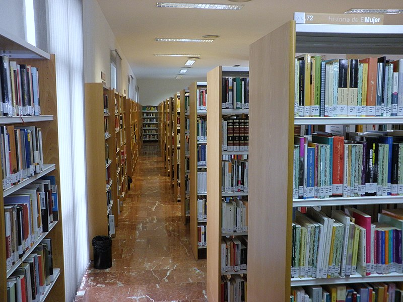 Imagen de los pasillos de una biblioteca en done se ve las estanterías con los libros clasificados.