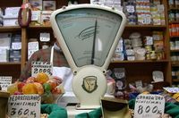 Tienda de comestibles donde aparece en primer plano una báscula antigua y de fondo una estantería llena de productos.