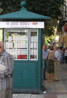 En esta imagen puedes ver un quiosco que vende lotería en una calle muy transitada de una ciudad.