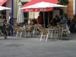 Imagen de una terraza de un bar. Se ven mesas y sillas, cubiertas con sombrillas, y a varias personas sentadas, disfrutando de un rato de ocio.  