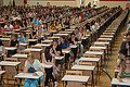Foto en la que aparecen los aspirantes participantes en una oposición en una gran sala preparada para realizar las pruebas.