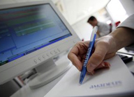 Mano de una persona con un bolígrafo frente al monitor de un ordenador.