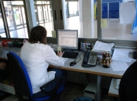 Frente al ordenador. Se observa a una administrativa desde la parte posterior sentada frente a su puesto de trabajo.