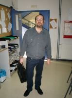 Jorge. En la imagen se observa a un hombre de pie, con pantalones vaqueros y camisa de manga larga con un maletín en la mano.