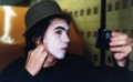 Mimo. Primer plano de un mimo con sombrero, el cual se está maquillando la cara de color blanco.