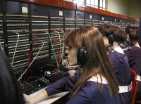 Operadoras. Se observan varios maniquíes de operadoras sentadas frente a un panel de comunicaciones.  Todas llevan auriculares en la cabeza y visten de azul.