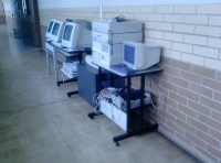 Ordenadores. Se muestra un conjunto de torres, monitores e impresoras amontonados en un pasillo.