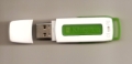Memoria. Se muestra una memoria externa tipo usb de color blanco.  Se encuentra en primer lugar el tapón o capuchón de la memoria y justo a su lado en posición tumbada la memoria externa, la cual tiene una zona de color verde en el centro.