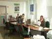 En la imagen se observa una oficina bancaria, donde frente a la cámara se encuentran tres agentes, dos mujeres y un hombre, en sus puestos de trabajo. Todos ellos llevan trajes de chaqueta y miran sonrientes.