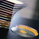 Varios cajetines de cd´s y un cd fuera de su caja sobre una mesa.