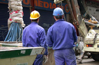 Dos obreros en una obra con ropa de trabajo azul y casco de protección.