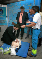 Un hombre hace prácticas de reanimación cardiopulmonar sobre un maniquí, bajo la supervisión de un técnico en emergencias que le da explicaciones, mientras otras tres personas le observan.