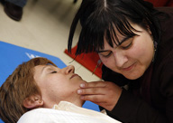 Foto de una mujer con la cabeza inclinada sobre la cara de otra,  comprobando la respiración de la paciente, que está tendida en el suelo.