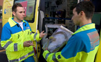 Junto a una ambulancia dos técnicos de emergencias, con su indumentaria de trabajo, hablando.