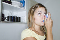 Silvia está administrándose un aerosol que sostiene con una mano manteniendo el aerosol en su boca.