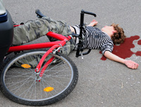 Fotografía en la que se ve un chico joven que está  inconsciente en el suelo. Una bicicleta está sobre sus piernas y alrededor de su cabeza se ha formado una gran mancha de sangre.