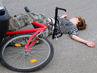 Fotografía en la que se ve un chico joven que está  inconsciente en el suelo. Una bicicleta está sobre sus piernas.