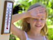 Fotografía de un termómetro que marca elevada temperatura. Al fondo una niña vestida con ropa de verano se lleva la mano a la frente con gesto cansado.