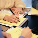 Persona rellenando un documento en una reunión de trabajo.