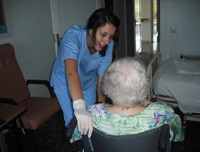 Profesional de centro residencial comunicando algo a una paciente anciana en silla de ruedas.