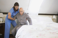 Imagen de una cuidadora ayudando a levantarse de la cama a un anciano dependiente.