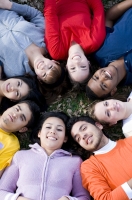 Fotografía de las caras de un grupo de jóvenes de etnias diferentes, tumbados sobre la hierba, formando un círculo, que representa la diversidad de las personas.