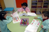 Fotografía de dos niñas y un niño sentados a la mesa en un aula interrelacionándose entre sí.