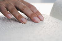 Fotografía que muestra un libro escrito en lenguaje Braille para ciegos y, sobre él una mano en gesto de lectura.