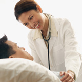 Fotografía de una médica atendiendo a su paciente en la cama, mirándole a los ojos y sonrriéndole.