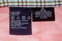 Etiqueta negra de ropa cosida a una prenda de cuadros, colocado sobre una superficie rosa, pueden verse las instrucciones de lavado y planchado, lugar de fabricación, etc.