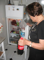 Junto a una nevera con la puerta abierta, llena de productos alimenticios de todo tipo, dispuestos en baldas. María (72 años, pelo pintado de castaño y vestido negro) observa de perfil lo que hay dentro y en una de sus manos sostiene una botella grande de refresco de cola.