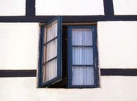 Fachada de una casa blanca con molduras marrones en la que puede verse una ventana de cristales y madera de color marrón oscura que permanece abierta.