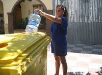 Esther (22 años, rubia, pelo recogido en una coleta. Con un vestido azul ) está en la calle echando una botella de plástico en un contenedor amarillo.