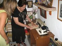 María (79 años, pelo corto y vestido negro) y Esther (22 años, pelo rubio largo y vestido verde) se inclinan a mirar una máquina de coser.