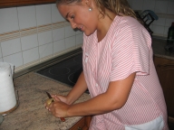 Esther 22 años, rubia, pelo largo recogido en una coleta y uniforme de TAPD de rayas rosas. De pie en la cocina. Pela una patata sobre la encimera.