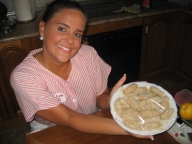 Esther, 22 años, rubia, pelo largo recogido en una coleta y uniforme de TAPD de rayas rosas. En la cocina, muestra sonriente a la cámara un plato de croquetas elaboradas, listas para freír.