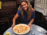 Esther 22 años, rubia, pelo largo y rizado con espuma, con un vestido azul. Muestra sonriente una ensaladilla rusa que está colocando en la mesa del comedor.