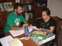 En el despacho de Leonardo.  Leonardo (chico de unos 36 años, moreno, con barba y camiseta verde) coloca sus papeles, este charla animadamente con María, mujer de 79 años con el cabello corto, teñido de negro. Y un vestido también negro.