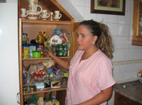 Esther. Una chica de 22 años. Es rubia con el pelo largo, lo tiene recogido hacia atrás y rizado con espuma. Tiene dos perlas grandes blancas como pendientes y viste un uniforme a rayas rosas y blancas, está en la cocina junto a una despensa abierta.